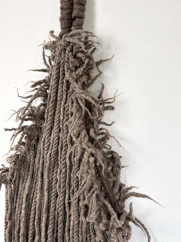 Textured wall hanging with frayed edges on a light gray background