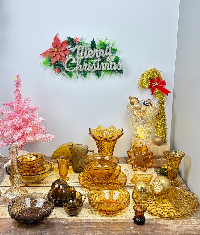 Vintage amber and smoky brown glass bowls, cups, vases and serving plates arranged on a rustic table for Christmas.