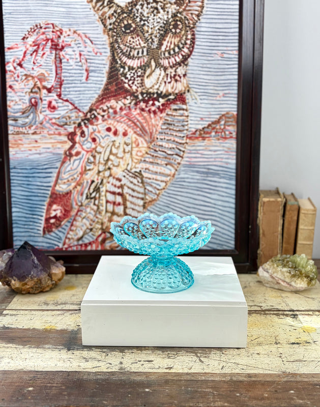Aqua Fenton hobnail glass candle holder displayed on a white plinth in front of framed owl artwork