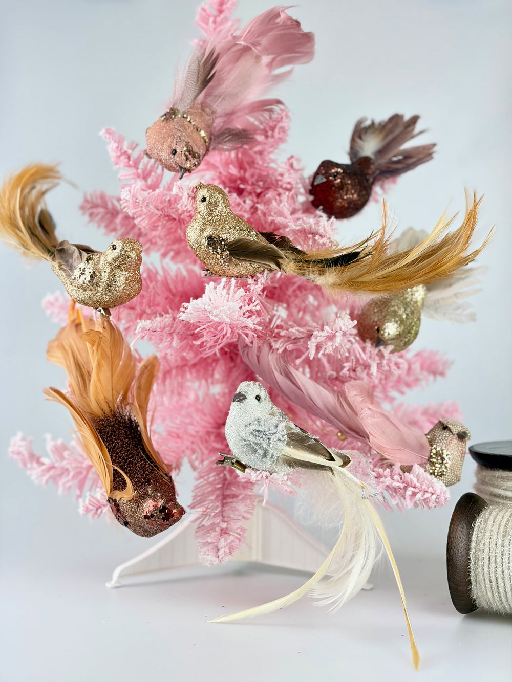 Decorative arrangement with vintage style pink coral and gold-feathered clip on birds on a pink Christmas tree with a white background.