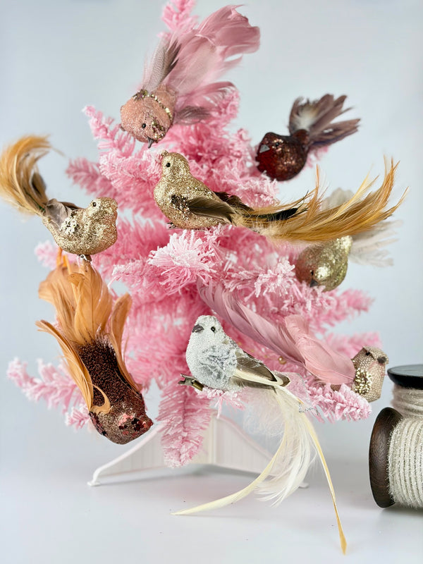 Decorative arrangement with vintage style pink coral and gold-feathered clip on birds on a pink Christmas tree with a white background.