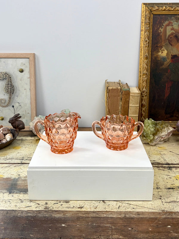 Indiana Glass Whitehall peach pink creamer jug and open sugar bowl displayed together on white box in artist's studio, styled with seahorse artwork, bronze rabbit, shells, aquamarine crystal and gilt-framed oil painting, circa 1960s–1980s