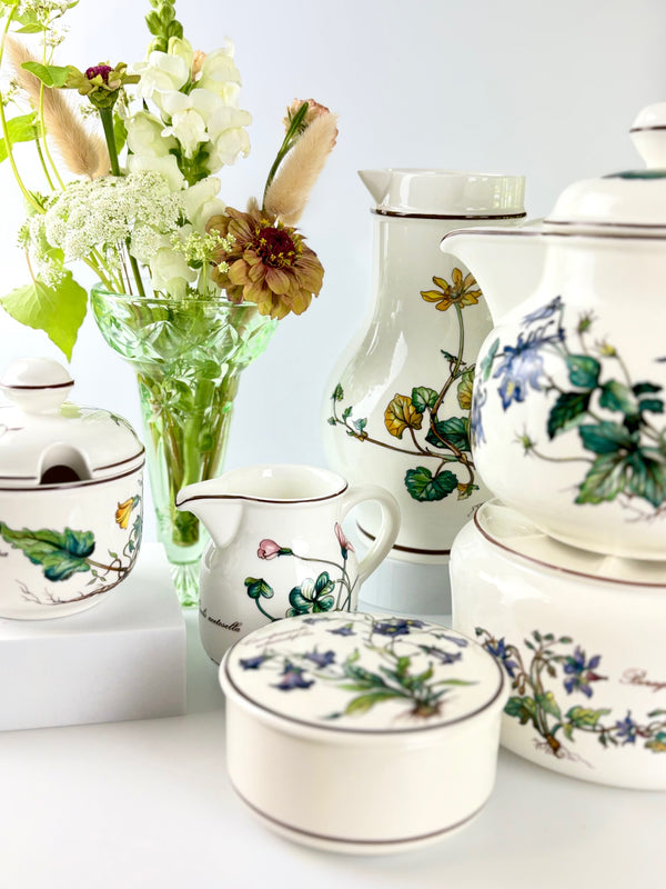 Collection of ceramic teapots and jugs with floral patterns on a white surface.